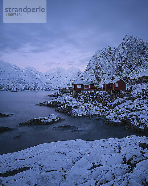 Rote Rorbu-Hütten an schneebedeckter Felsküste  Hamnøy  Lofoten  Norwegen