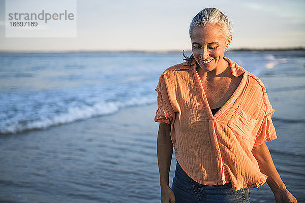 Grauhaarige Frau genießt den Strand bei Sonnenuntergang