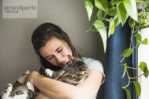 Frau zu Hause  die mit ihrer Katze am Fenster kuschelt