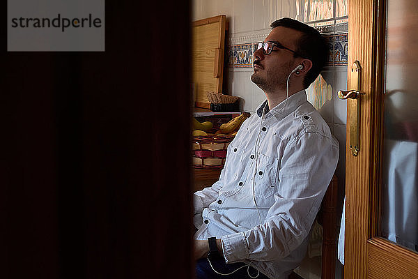 Ein junger Mann hört mit seinen Kopfhörern Musik  während er zu Hause sitzt