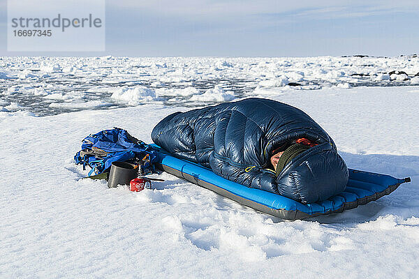 Männlicher Wanderer entspannt sich im Schlafsack auf einem schneebedeckten Berg