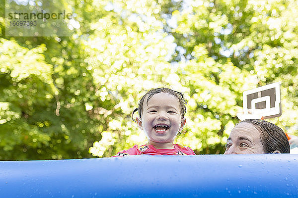 Glückliches Mädchen mit Mutter lächelnd beim Blick über Seite des aufblasbaren Pools