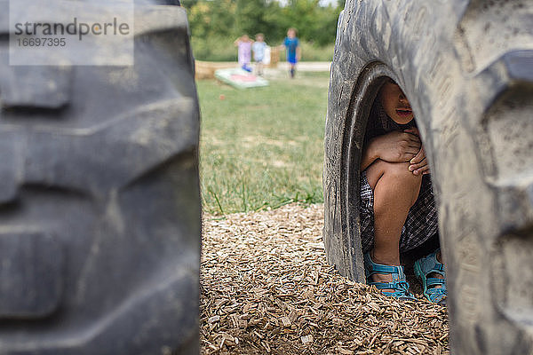 Ein Junge versteckt sich beim Versteckspiel in einem Reifen auf einem Spielplatz