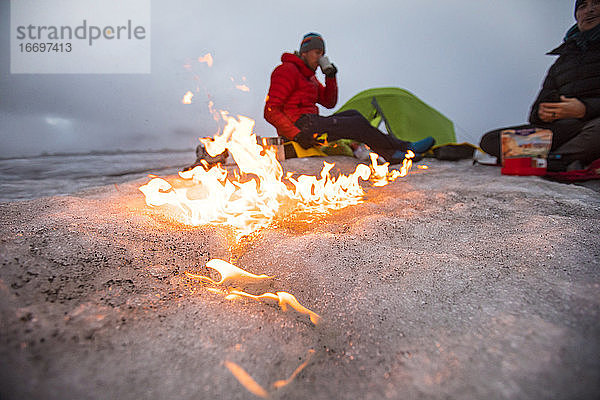 Ein Lagerfeuer zieht über den Gletscher  während zwei Männer auf einem Gletscher kampieren.