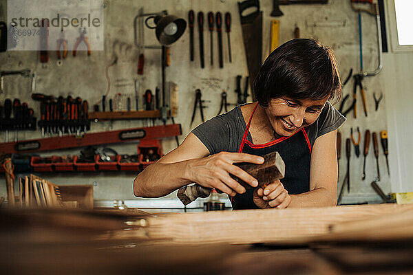 Holzarbeiterin bei der Arbeit in der Werkstatt  im Hintergrund hängen Werkzeuge