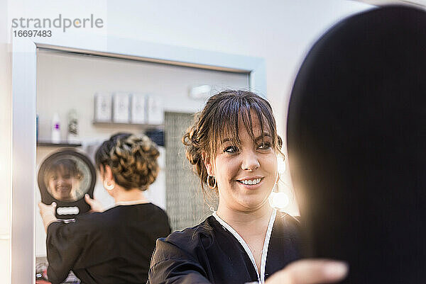 Lächelnde Frau  die sich im Friseursalon im Spiegel betrachtet