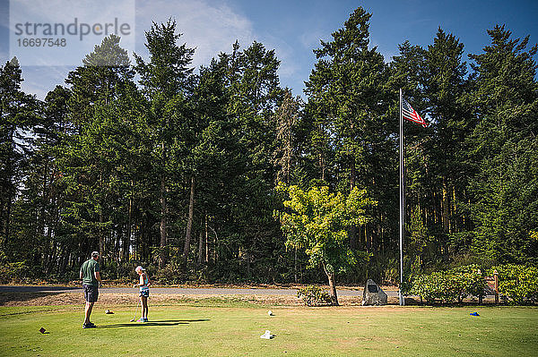 Mann und junges Mädchen am Golfabschlag mit amerikanischer Flagge und Bäumen im Hintergrund