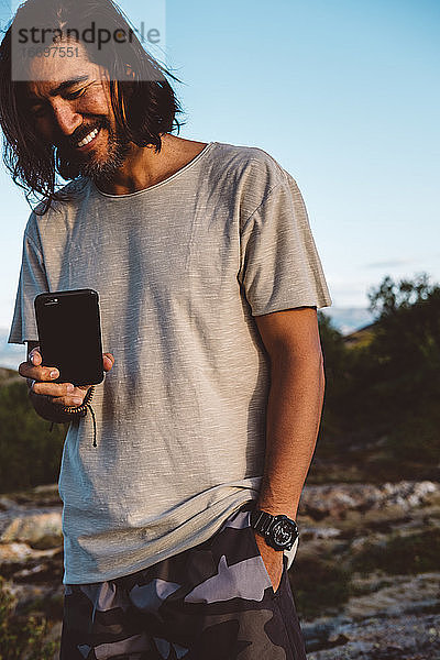 Lächelnder Mann  der ein Foto mit seinem Smartphone im Freien macht