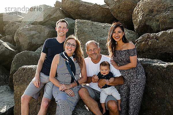 Fünfköpfige Familie lächelt für die Kamera auf Felsen am Strand sitzend