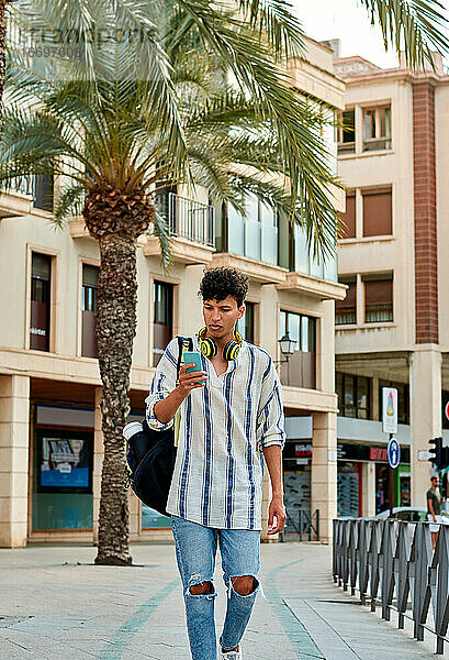 Junger afro-haariger Mann geht die Straße entlang und schaut auf sein Handy