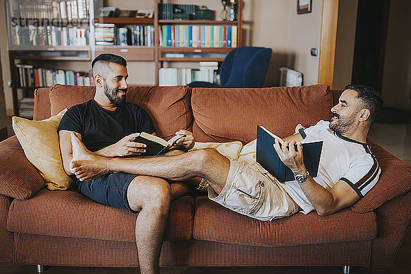 schwules Paar  das auf dem Sofa liest und die Beine übereinander schlägt