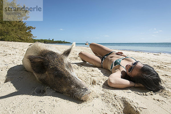 Junge Frau entspannt sich bei einem Schwein am Strand an einem sonnigen Tag