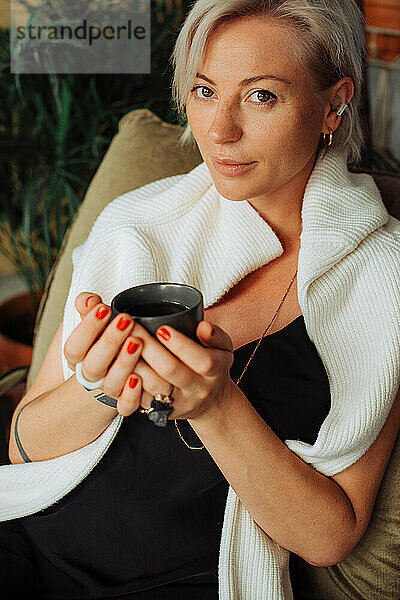 Stilvolle blonde Frau hält eine Tasse Kaffee  während sie in einem Café sitzt