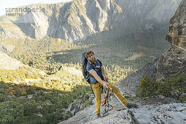 Mann jongliert mit Seil auf dem El Capitan und macht ein lustiges Gesicht mit Rucksack