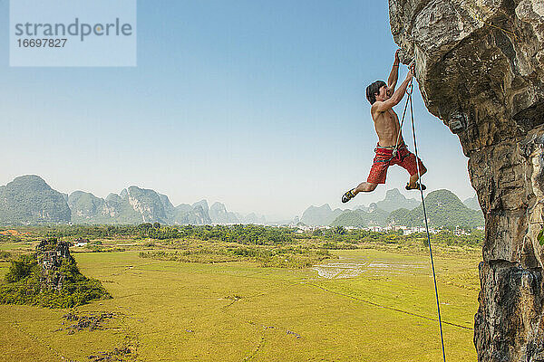 Männlicher Kletterer zieht sich an einem überhängenden Felsen in Yangshuo / China hoch