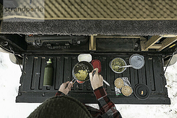 Draufsicht auf eine Frau  die im Kofferraum eines Geländewagens Essen zubereitet