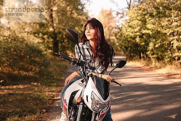 Glückliche selbstbewusste junge Frau  die auf einem Motorrad sitzend wegschaut
