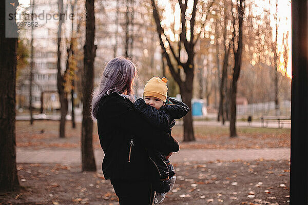 Mutter hält süßes Baby Sohn im Park im Herbst bei Sonnenuntergang