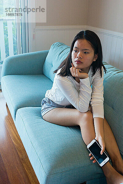 Asiatisches Teenager-Mädchen sitzt auf dem Sofa und sieht fern