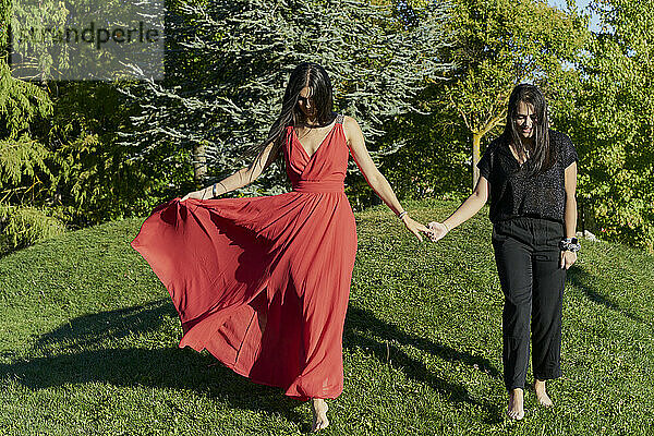 Junges lesbisches Paar  das sich an den Händen hält und auf grünem Gras in einem Park an einem sonnigen Tag spazieren geht. romantisches Konzept