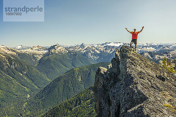 Ein Wanderer hebt nach dem Erreichen eines Berggipfels jubelnd die Hände.