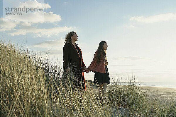 Mutter und Tochter am Strand stehend mit Blick aufs Meer