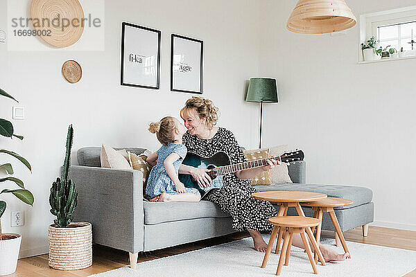 Mutter und Tochter saßen lachend zu Hause und spielten zusammen Gitarre
