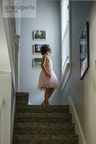 Ein kleines Mädchen in einem Kleid steht am oberen Ende der Treppe und schaut aus dem Fenster