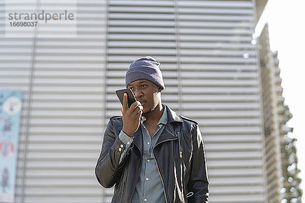 junger afrikanischer Mann in der Stadt  der mit seinem Smartphone telefoniert