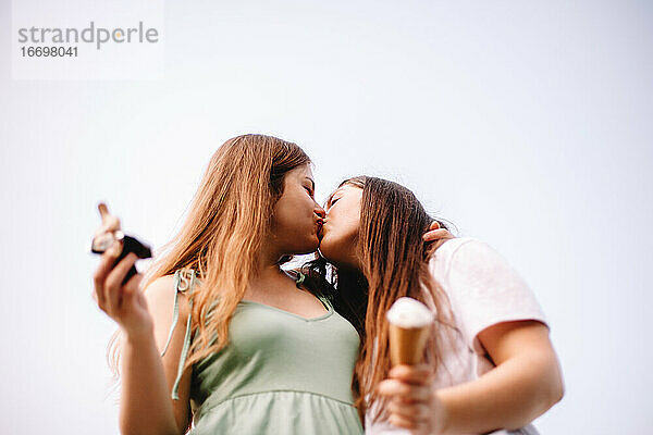Glückliches lesbisches Paar küsst stehend gegen den Himmel im Sommer