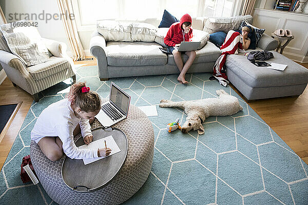 Wide View of Siblings in Living Room Doing School Arbeit auf Geräte