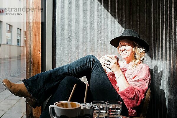 Frau sitzt lachend in einem Cafe und trinkt Kaffee in der Sonne