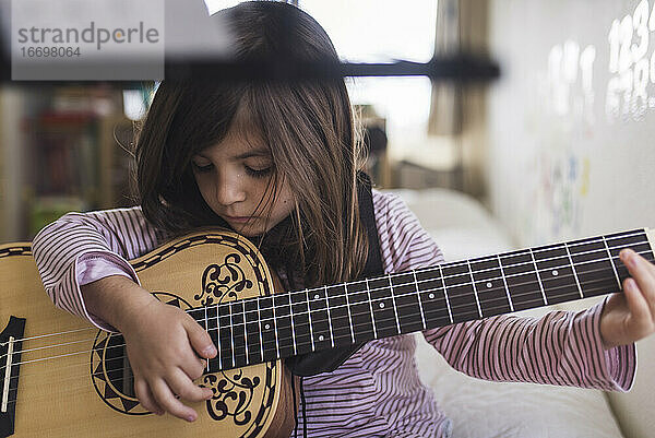 Konzentriertes junges Mädchen  das auf dem Bett sitzend Gitarre spielen lernt