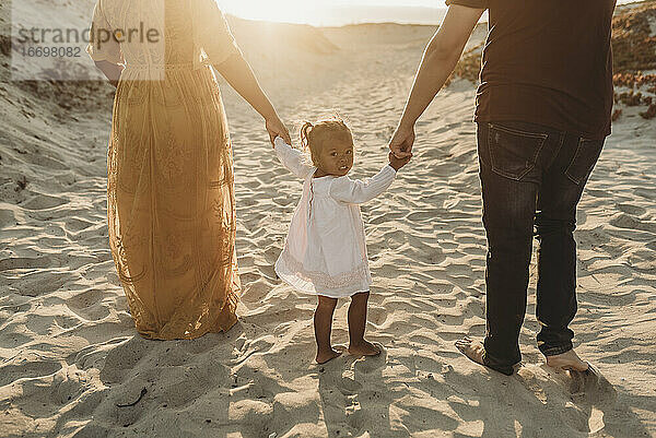 Hinteransicht einer jungen Familie  die bei Sonnenuntergang am Strand spazieren geht
