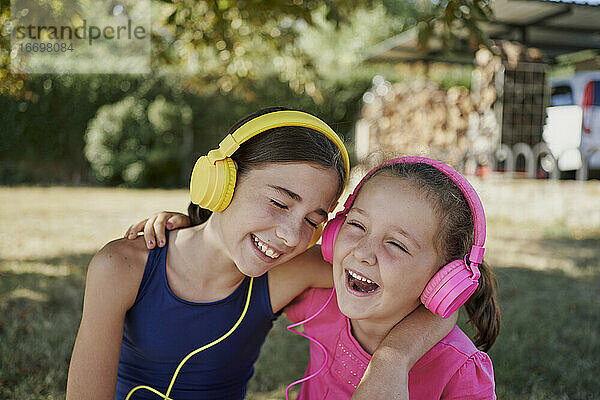 Kleine Mädchen hören Musik und lächeln mit gelben und rosa Kopfhörer in einem Garten. Musik-Konzept