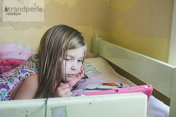 Junges Mädchen liegt auf ihrem Bett und schaut auf ihr Gerät
