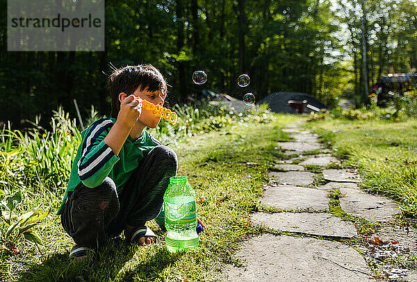 Kleiner Junge  der im Freien mit einem großen Stab Seifenblasen pustet.