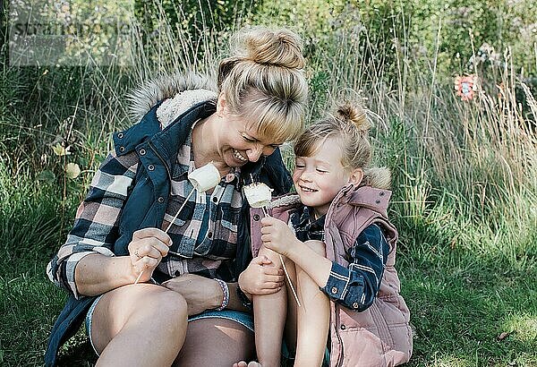 Mutter und Tochter rösten glücklich lächelnd gemeinsam Marshmallows