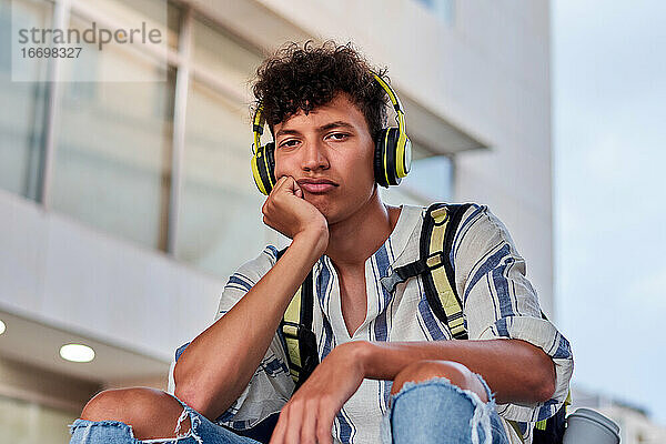 Langweiliger junger Afro mit Kopfhörern auf der Straße sitzend