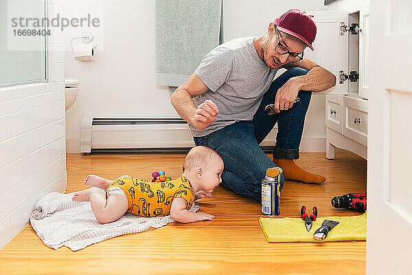 Vater repariert Küchenspüle  während das kleine Mädchen zu Hause auf dem Hartholzboden liegt