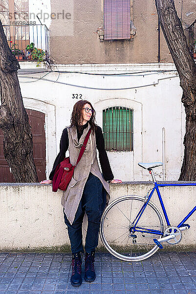 Junge Frau lehnt an einer Stadtmauer mit Vintage-Fahrrad in sonnigen Tag