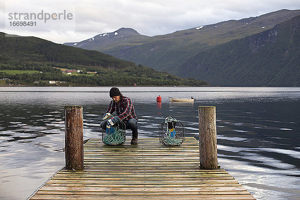 Ein Norweger bei der Arbeit mit Krabbenreusen auf einem Steg am Fjord
