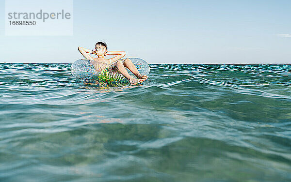 entspannter weißer Junge schwimmt in einem Schwimmer im Meer und genießt die ruhigen Wellen im Sommer