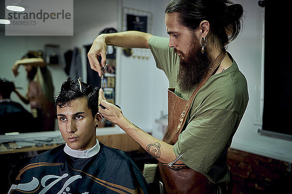 Ein bärtiger Mann schneidet einem modernen jungen Mann die Haare