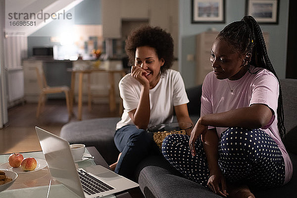 Charmante Damen  die einen Film auf einem Laptop genießen und eine Party zu Hause feiern