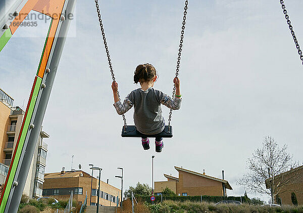 Rückansicht eines glücklichen kleinen Mädchens  das auf einer Spielplatzschaukel schwingt