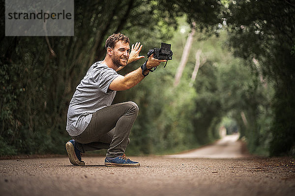 Lächelnder Fotograf macht Selfie auf einer Straße  wo Bäume einen Tunnel bilden
