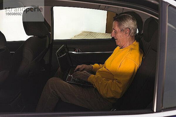 Ein älterer Mann benutzt einen Laptop auf dem Rücksitz des Autos