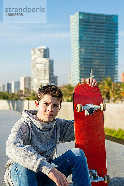 Teenager sitzt auf einer Skatepark-Rampe und hält ein Skateboard  schaut in die Kamera