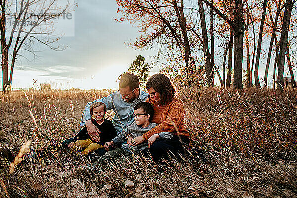 Lächelnde junge Familie  die an einem Herbstabend auf einem Feld kuschelt